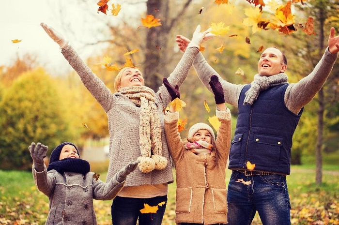 family of four wearing fall clothing throwing leaves into the air